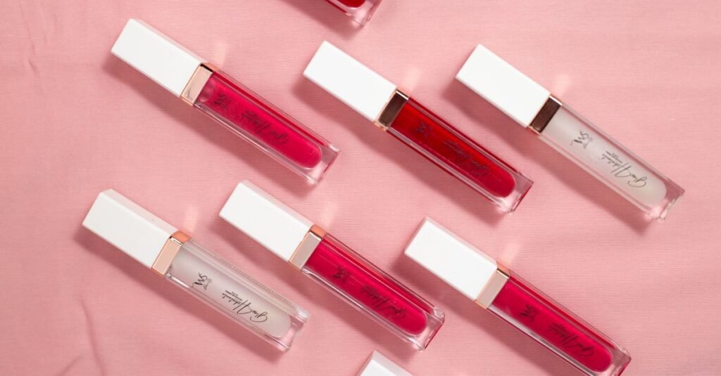 Colorful lip gloss tubes arranged on soft pink fabric background