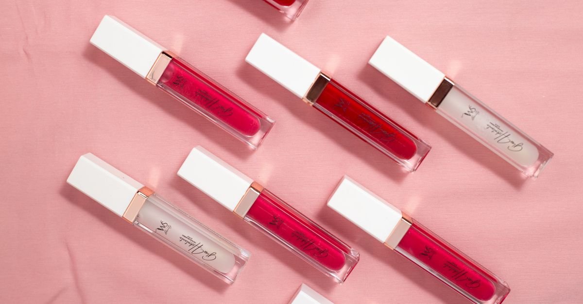 Colorful lip gloss tubes arranged on soft pink fabric background