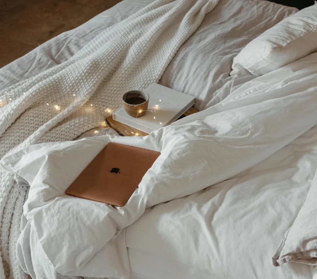 Cozy bed with laptop, books, and coffee for a fall movie night