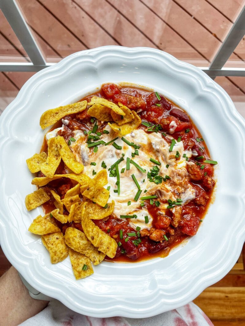 chili topped with sour cream, tortilla chips, and chives in a white bowl
