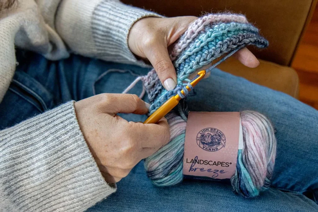 Hands crocheting multicolored yarn into a log cabin blanket square