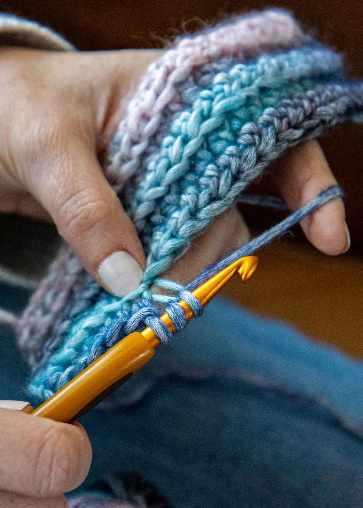 Close-up of hands working blue and pink yarn with a crochet hook